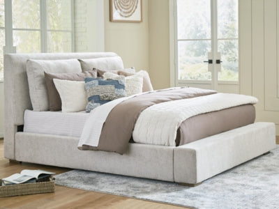 Ashley Furniture Cabalynn upholstered bed with a plush fabric headboard and wooden frame, shown in a modern bedroom setting.
